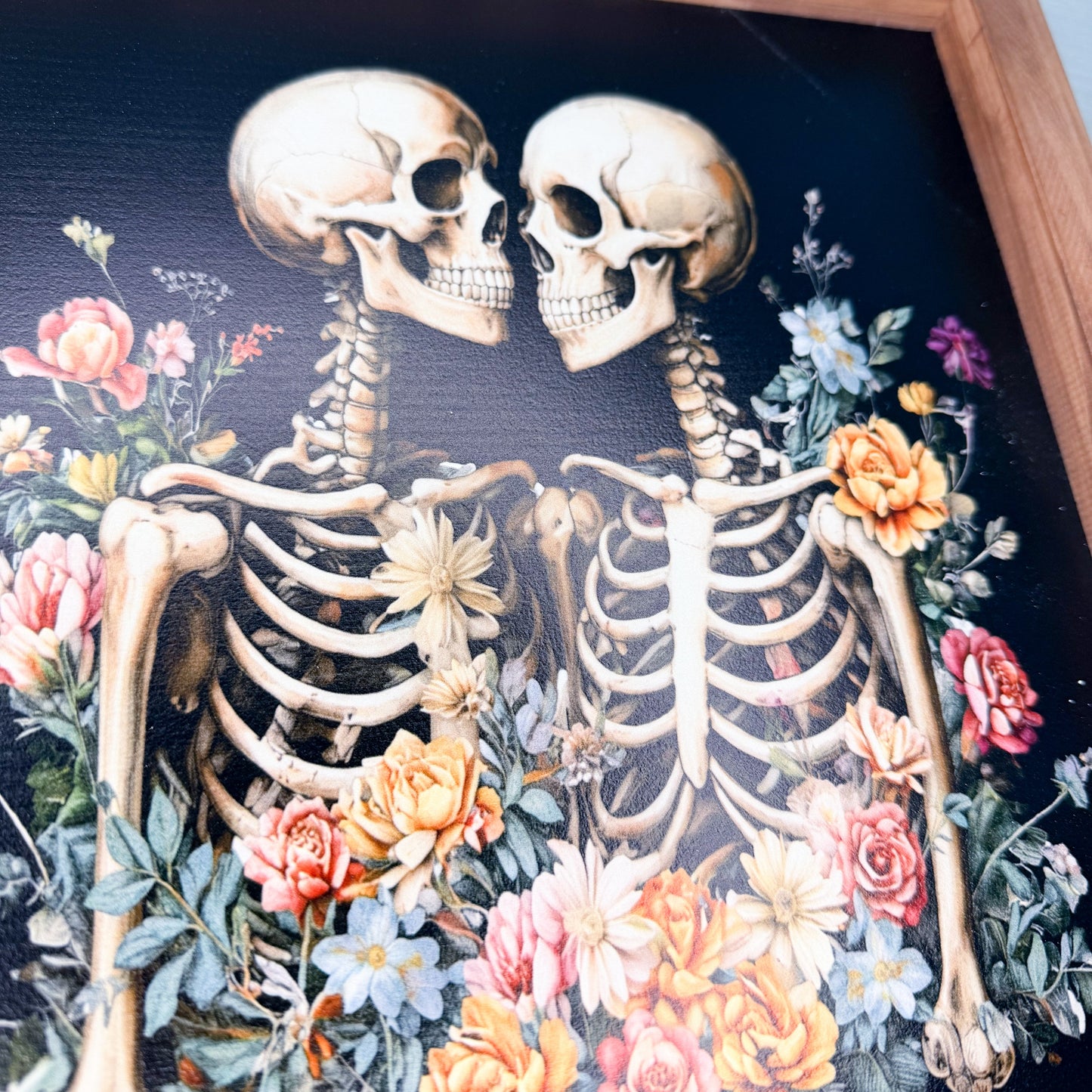 Two kissing skeletons surrounded by flowers on a dark background