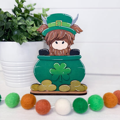 Decorative item with a leprechaun in a pot of gold on a white surface with plants and colorful balls.