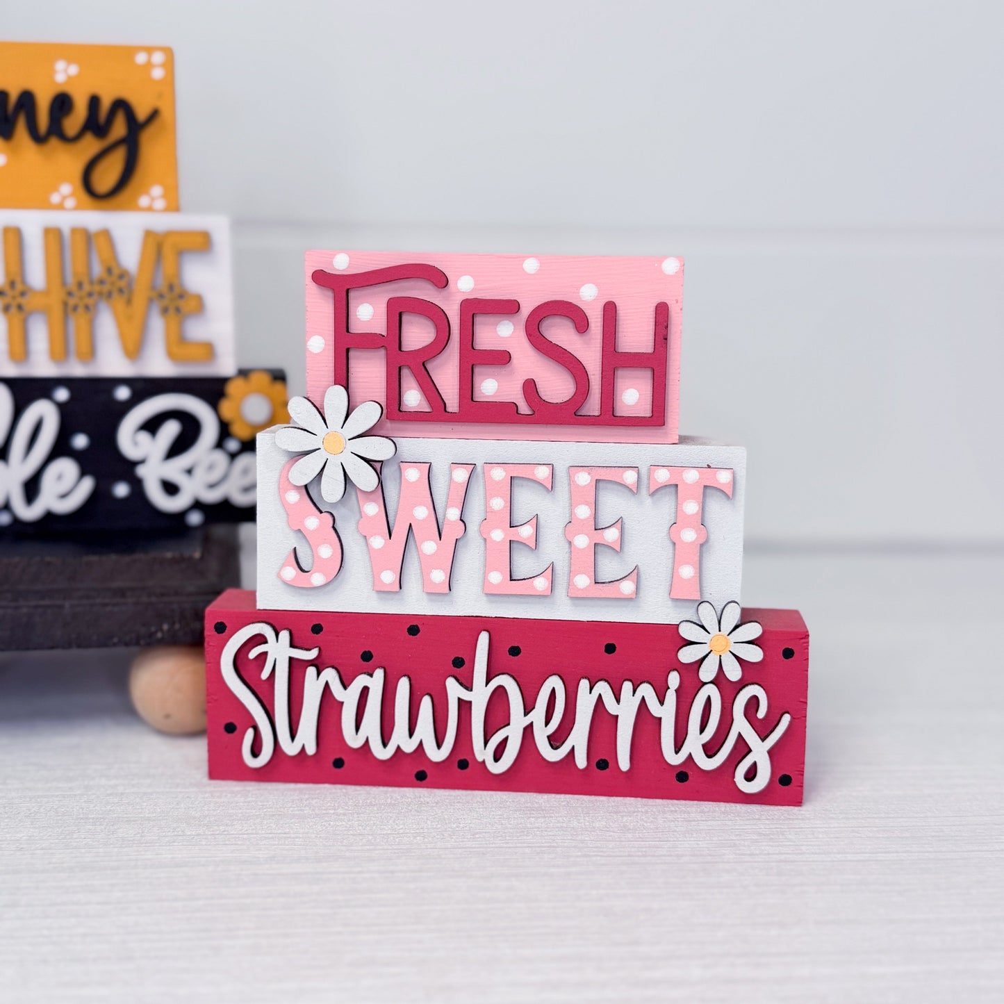 Stack of decorative wooden signs with 'Fresh Sweet Strawberries' text on a light gray background.