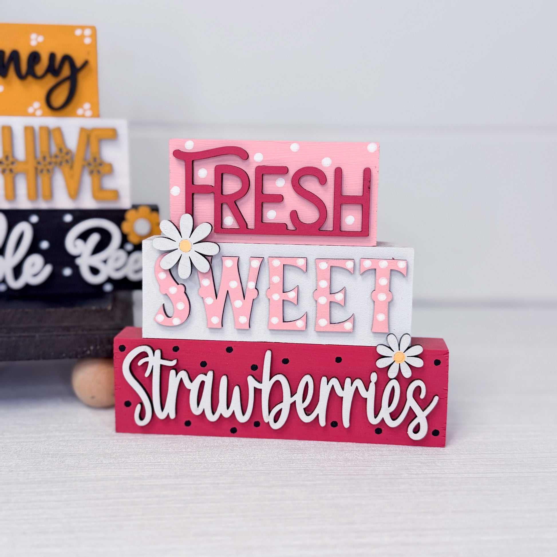 Stack of decorative wooden signs with 'Fresh Sweet Strawberries' text on a light gray background.