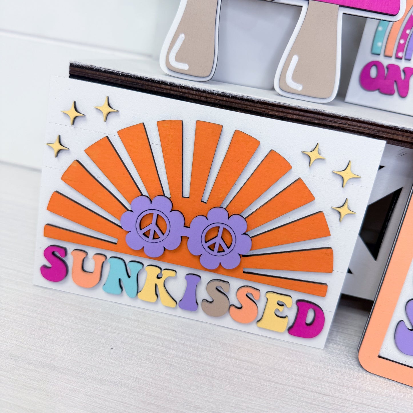 Colorful die-cut card with 'sunkissed' text and peace signs on a white surface.