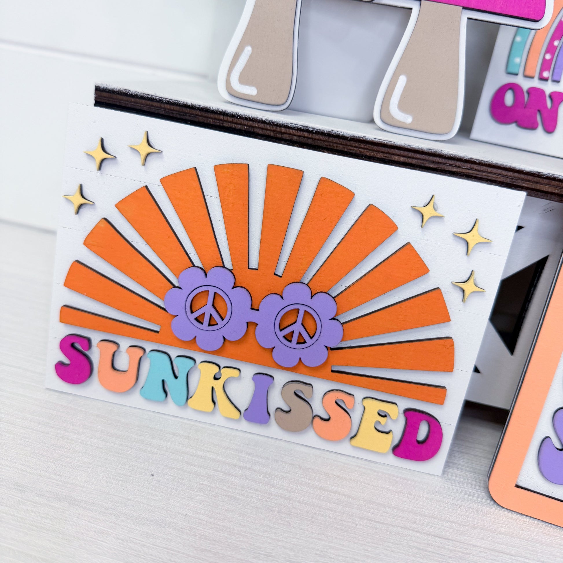 Colorful die-cut card with 'sunkissed' text and peace signs on a white surface.
