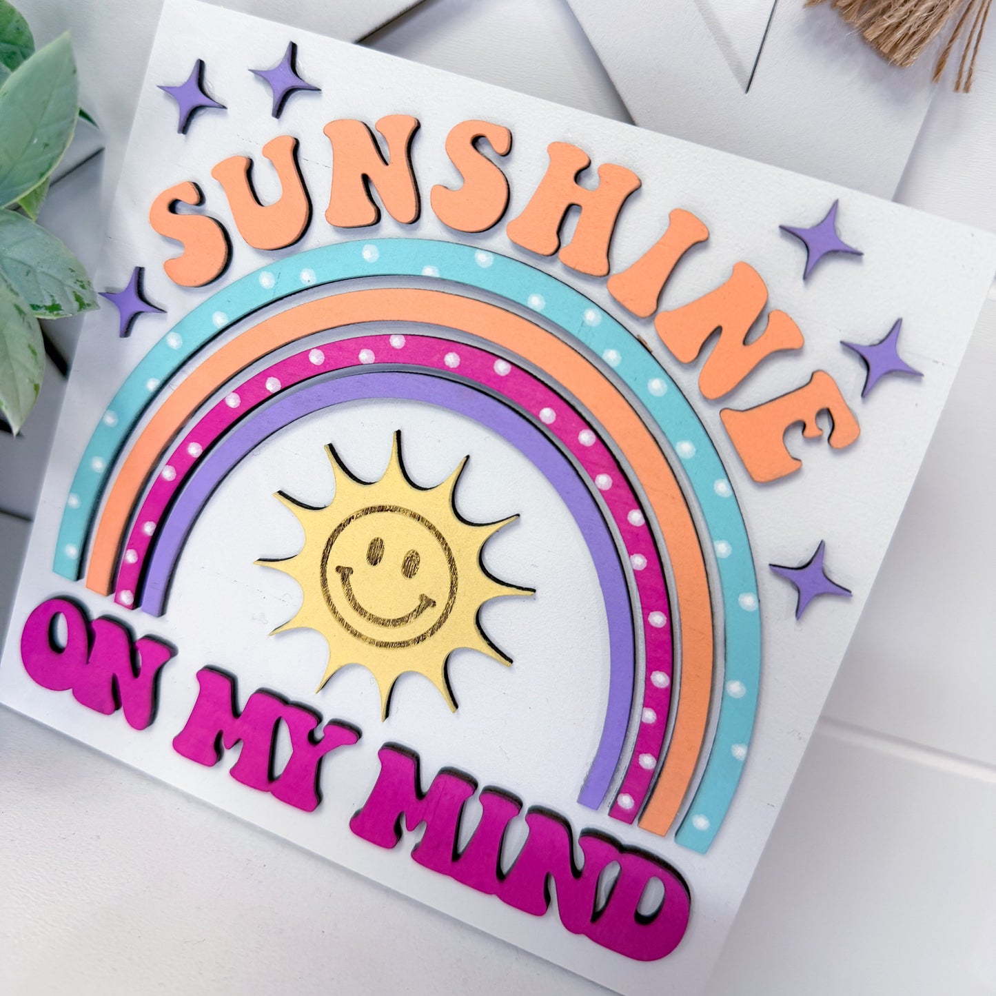 Decorative sign with rainbow and sun design on a white background