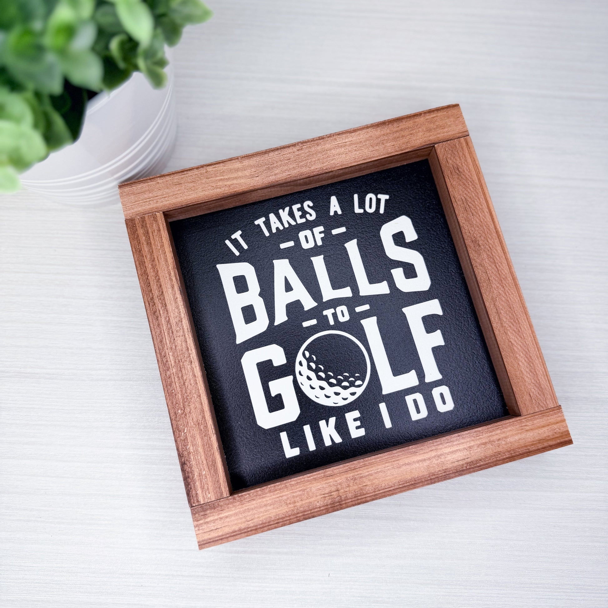 Wooden-framed sign with humorous golf quote on a white surface