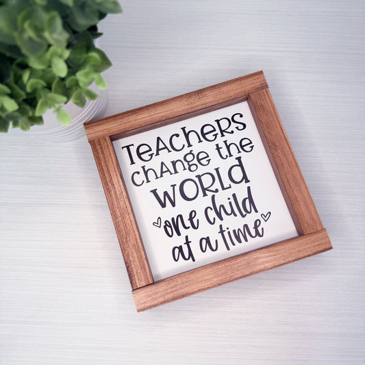Wooden-framed sign with 'Teachers change the world one child at a time' text on a light background