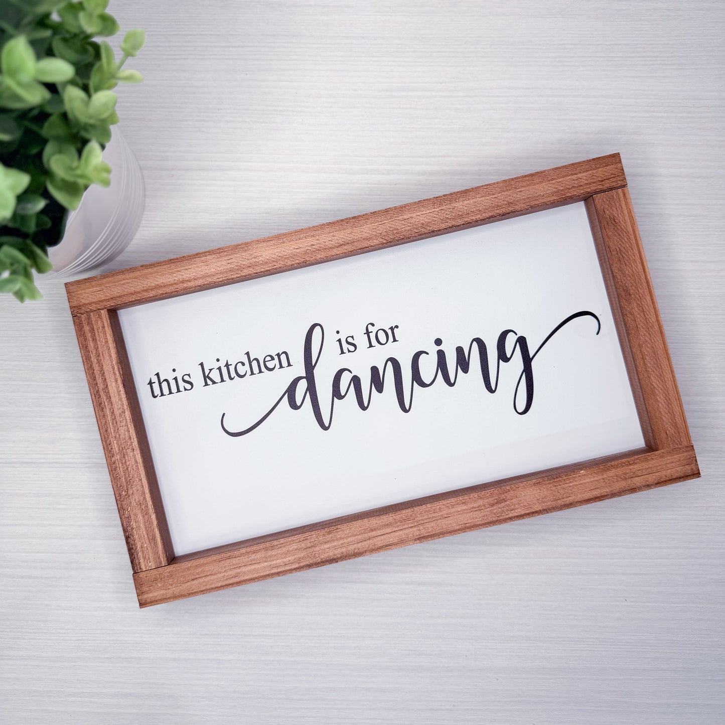 Wooden-framed sign with 'this kitchen is for dancing' text on a white background