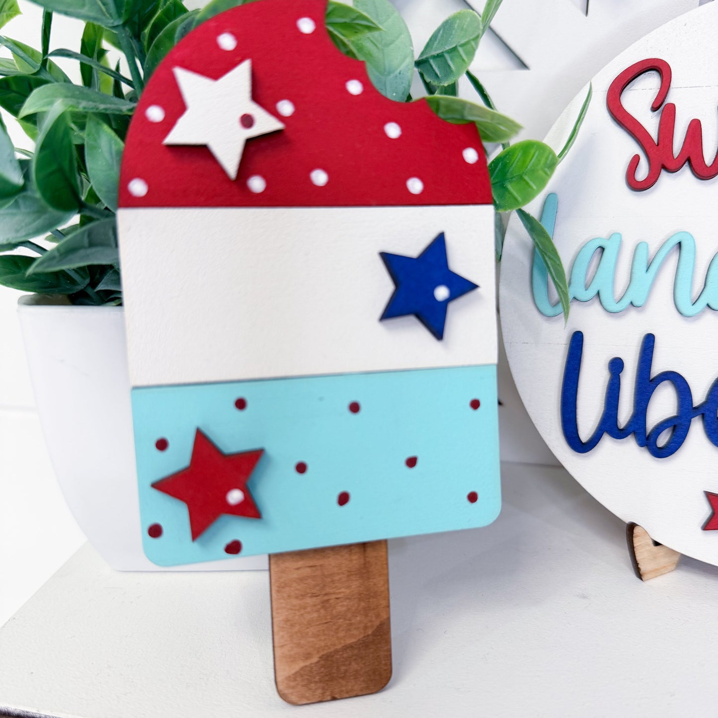 Decorative popsicle with red, white, and blue stars on a white surface with greenery.