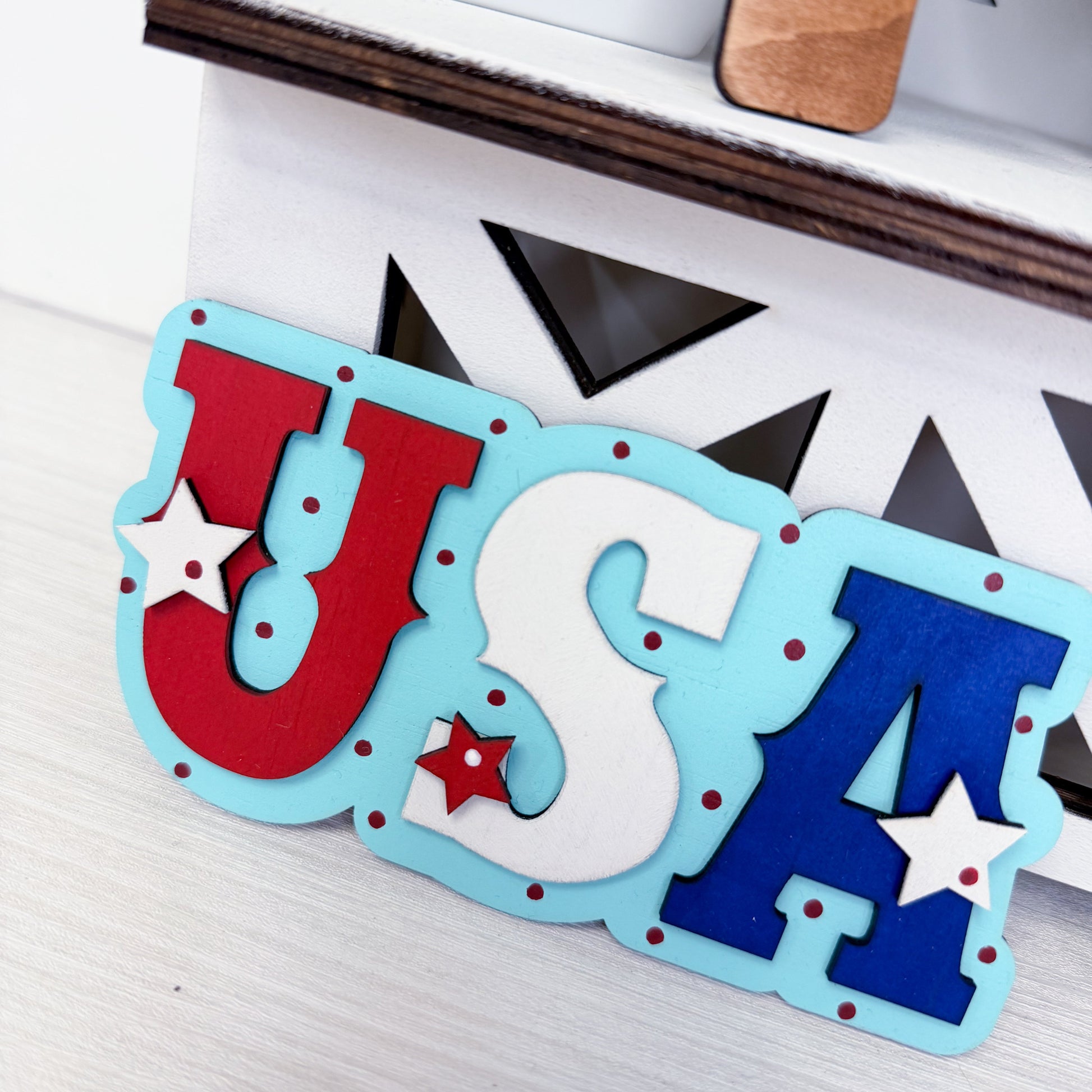 Decorative sign with 'USA' letters in red, white, and blue on a wooden surface.