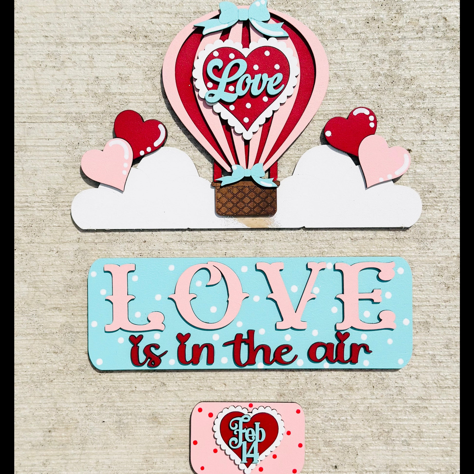 Valentine's Day-themed decor with hot air balloon, hearts, and 'Love is in the air' sign on a textured background.