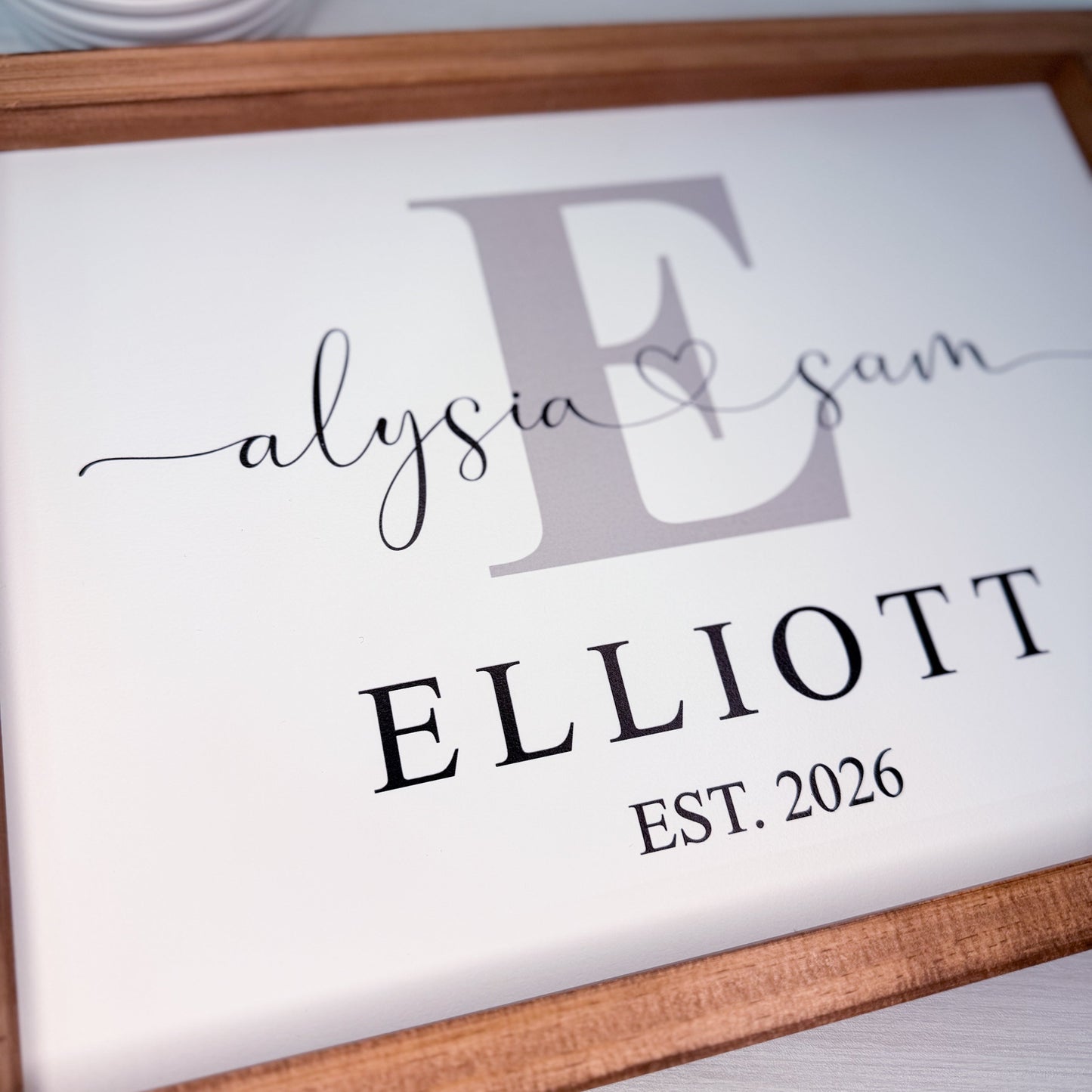 Personalized sign with 'Elysa & Sam' and 'ELLIOTT EST. 2026' text in a wooden frame.