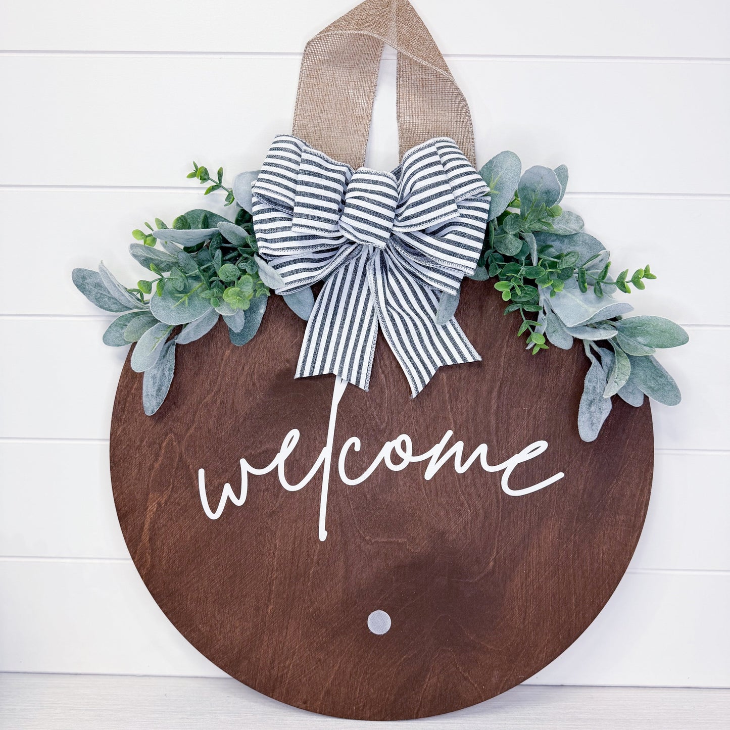 Wooden door hanger with 'welcome' text, striped bow, and greenery on a white background