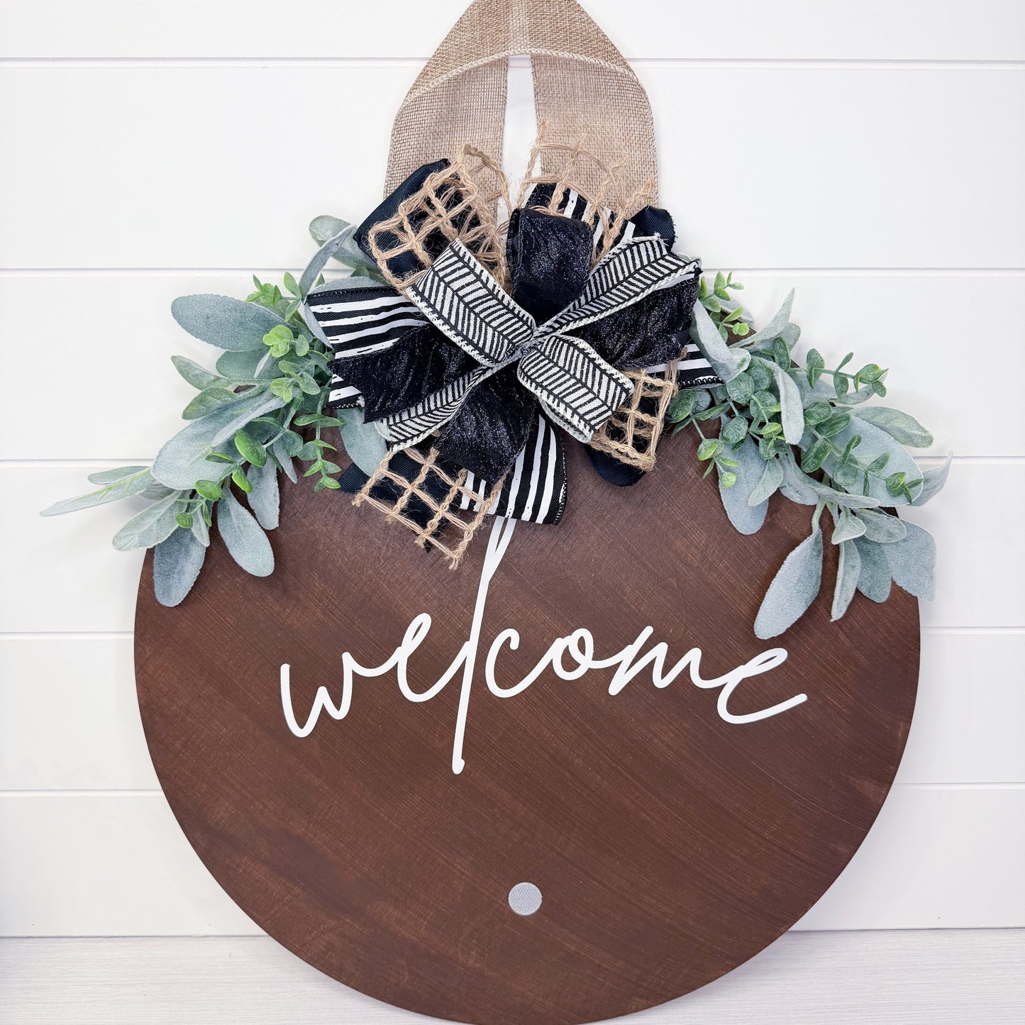 Decorative wooden sign with 'welcome' text, greenery, and a bow on a white background