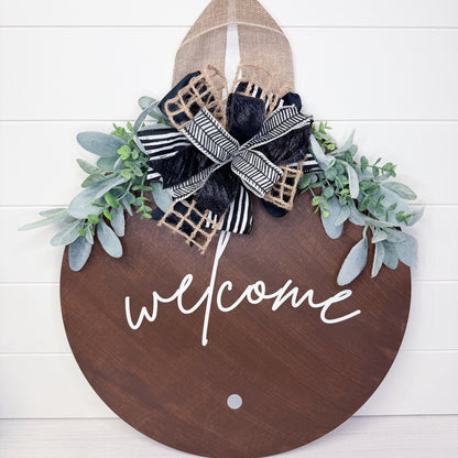 Decorative wooden sign with 'welcome' text, greenery, and a bow on a white background