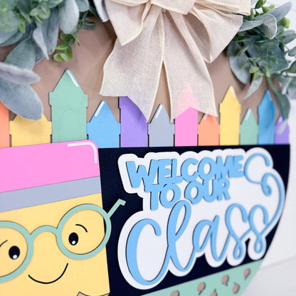 Decorative wreath with colorful crayons, a smiling face, and 'Welcome to our Class' text.