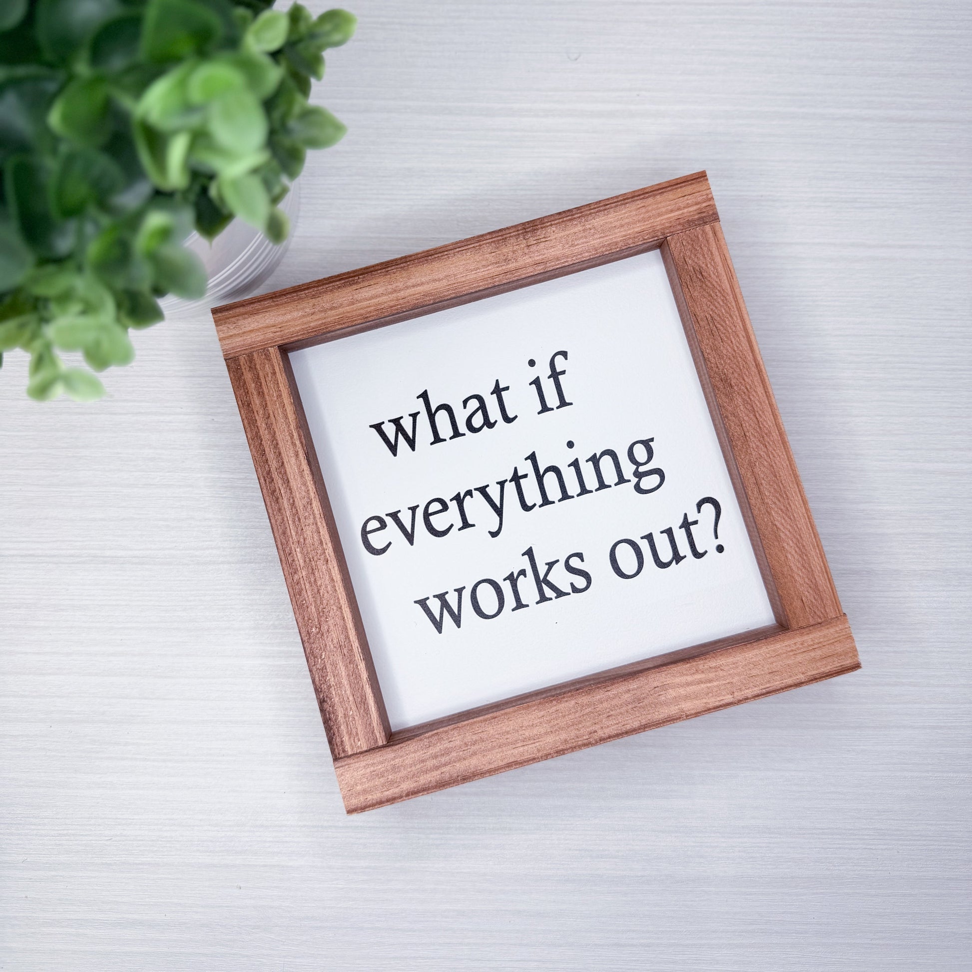 Wooden frame with a motivational quote 'What if everything works out?' on a light background.