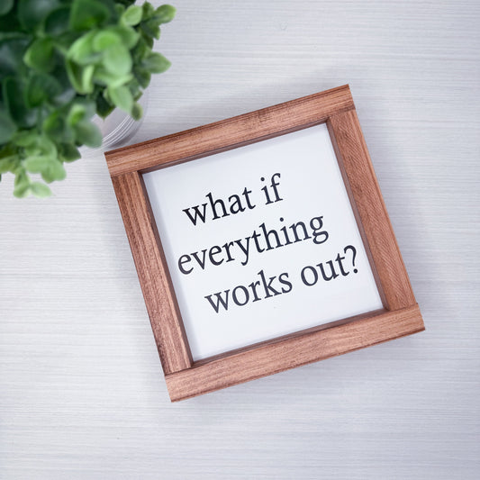 Wooden frame with a motivational quote 'What if everything works out?' on a light background.