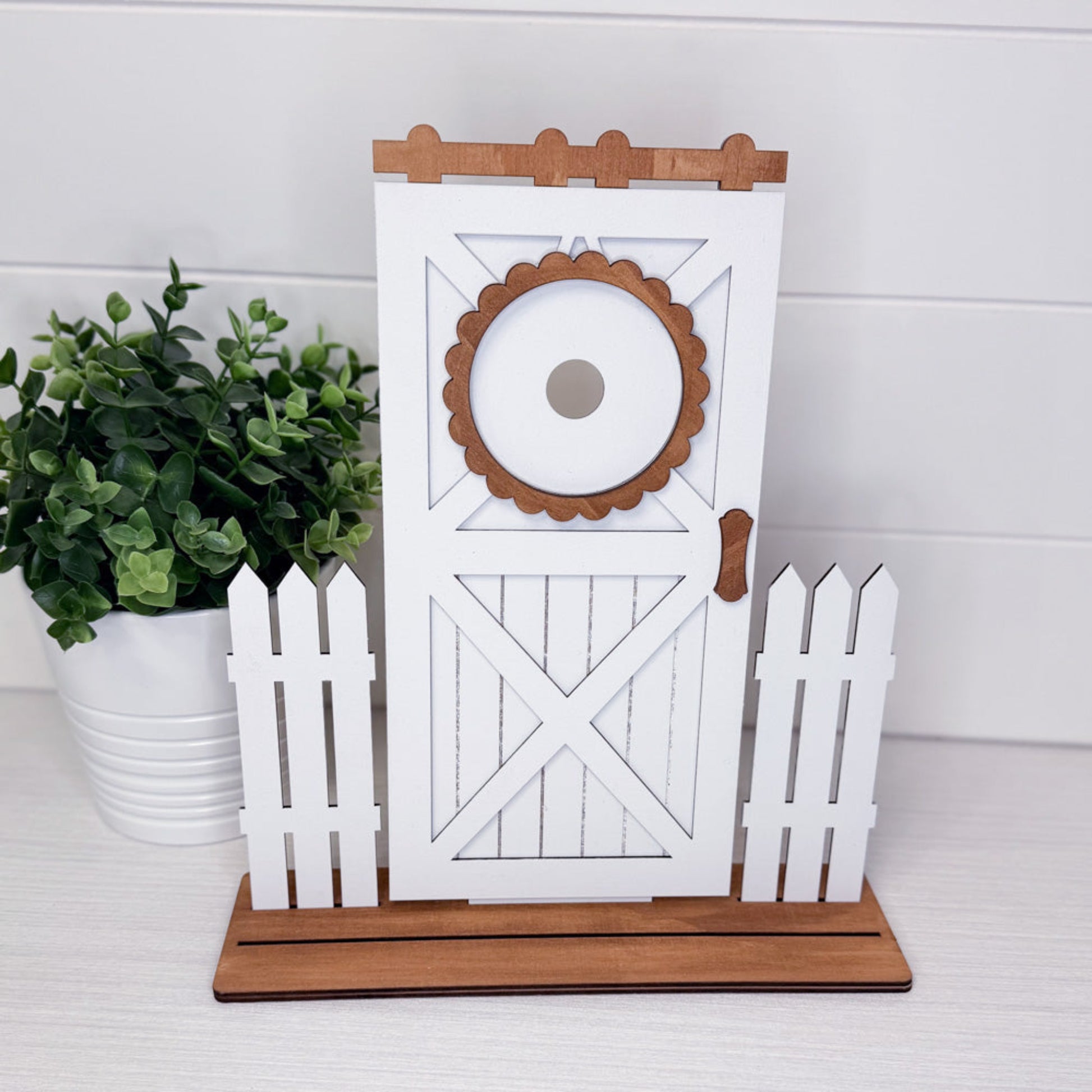 Decorative stand with white wooden design and brown accents, featuring a plant on a white surface.