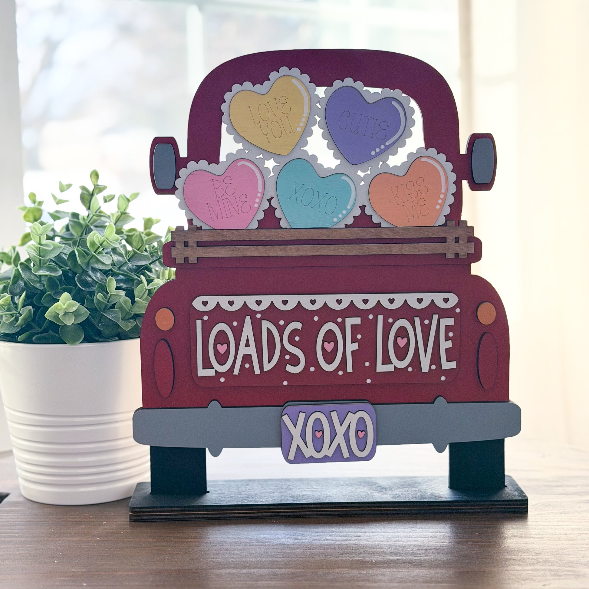 Decorative wooden truck with heart-shaped signs and 'LOADS OF LOVE XOXO' text on a wooden surface.